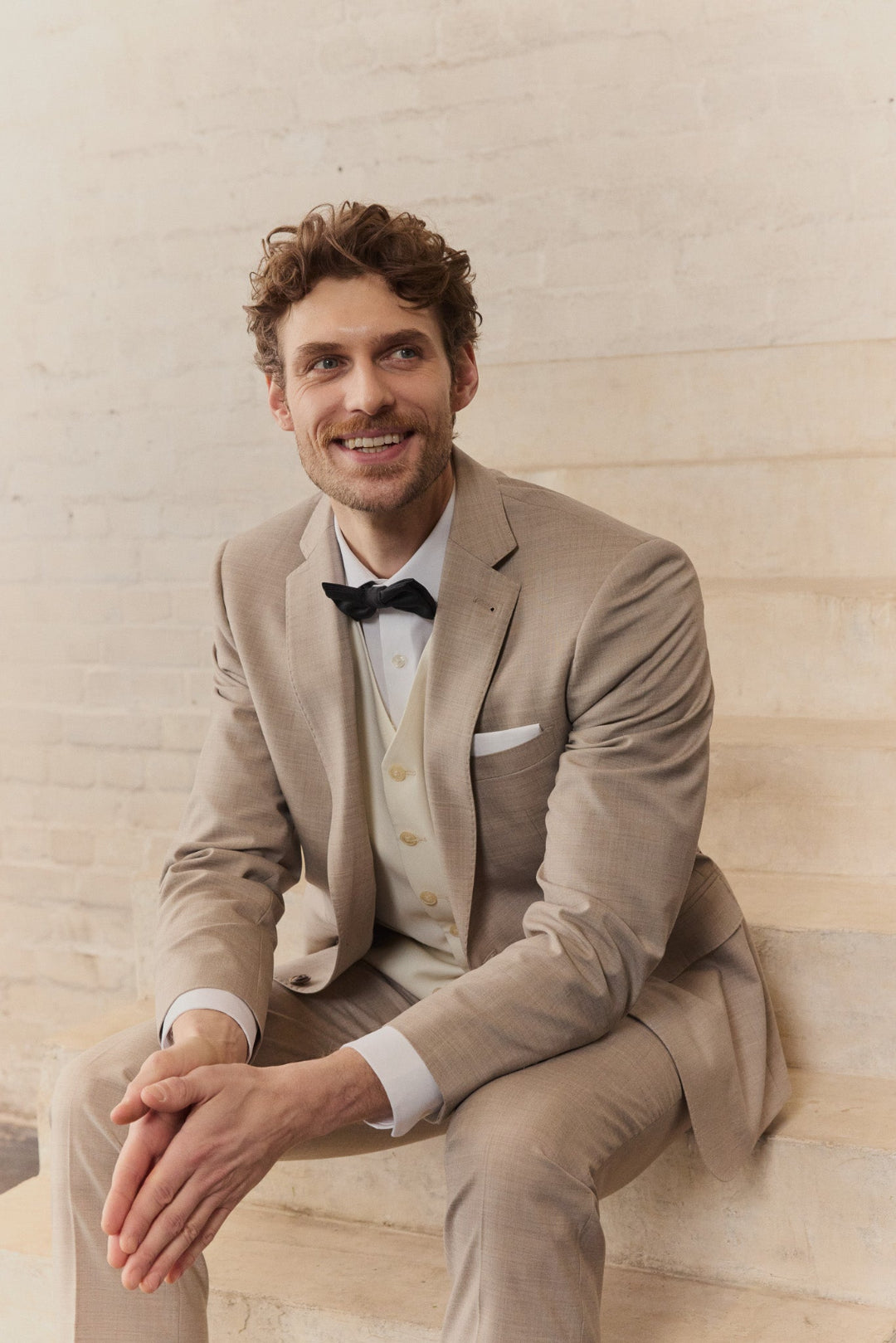 Ein Mann in einem hellen Hochzeitsanzug mit Weste und Fliege