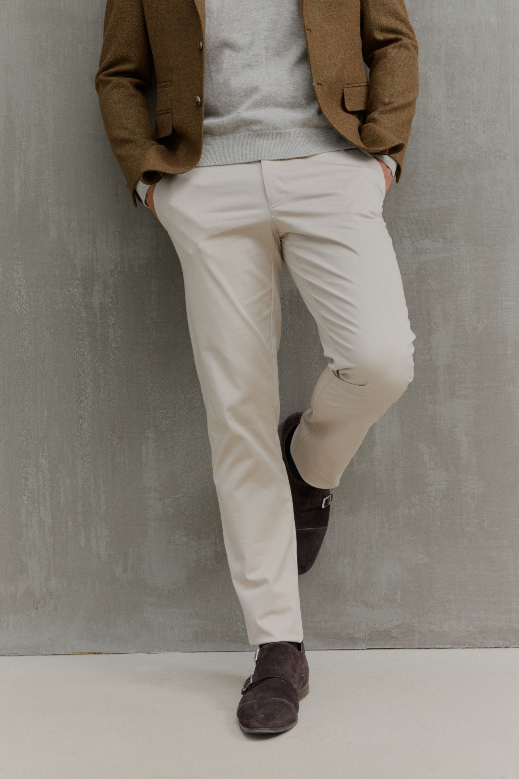 Mann trägt braune Jacke, grauen Pullover, beige Hose.