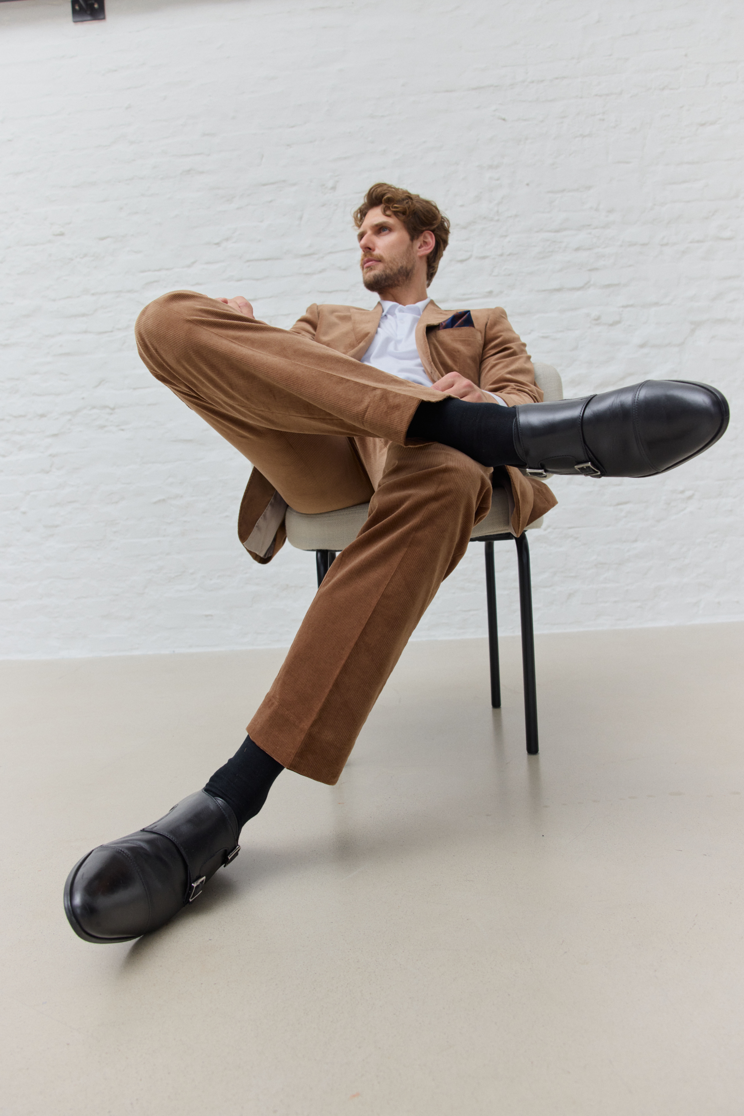 Mann in braunem Anzug sitzt auf Stuhl, schwarze Schuhe.