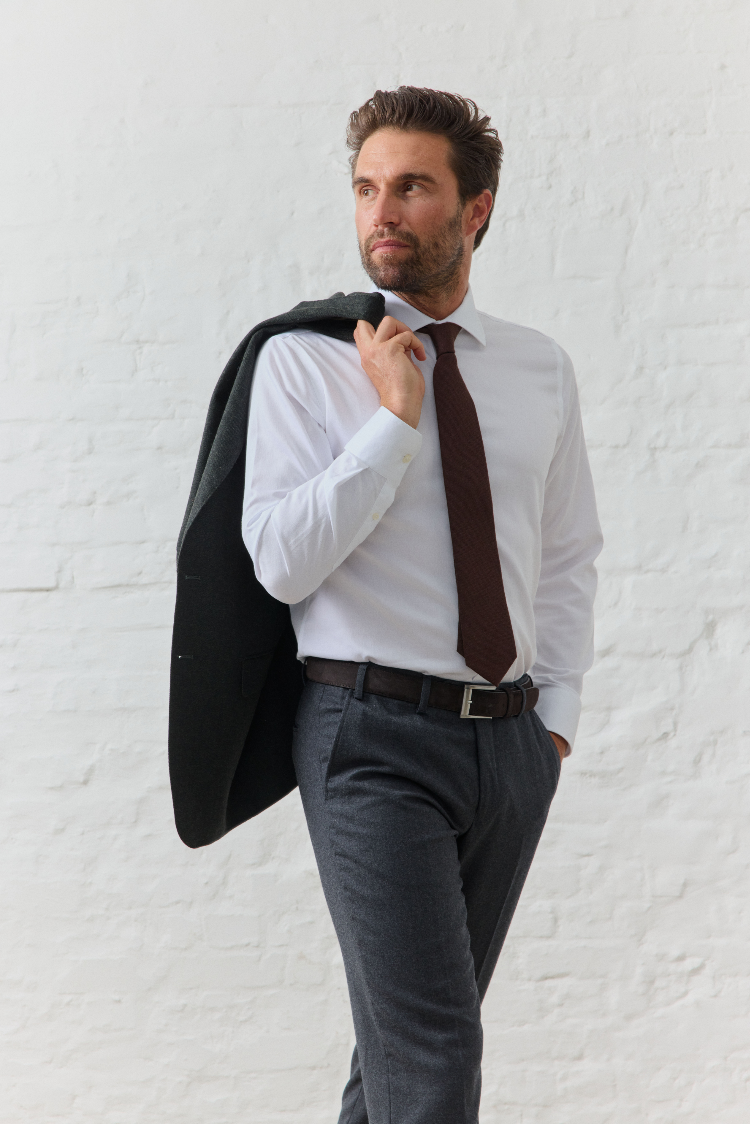 Mann in Anzug mit Jacke über Schulter, weißer Hintergrund.