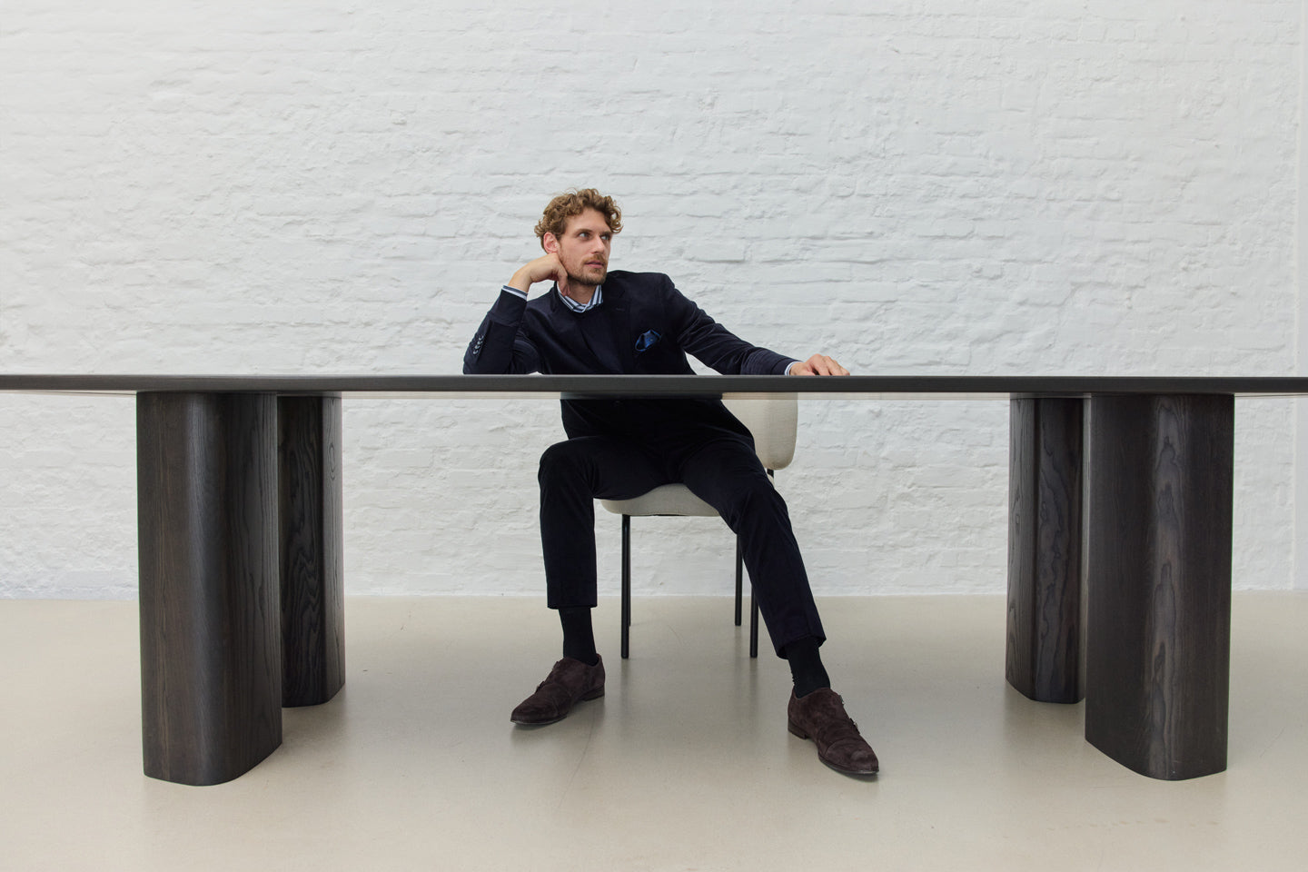 Mann in Anzug sitzt an großem Tisch, weiße Wand.