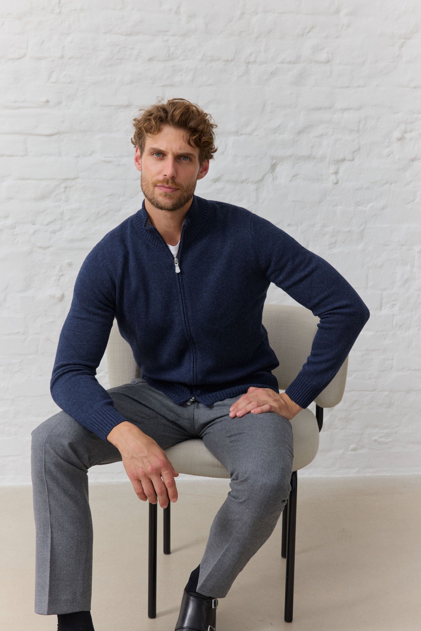 Mann in blauer Jacke und grauer Hose auf Stuhl.