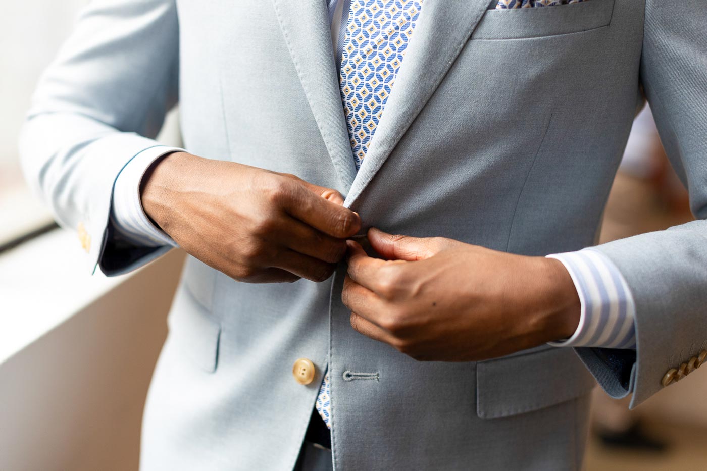 Mann knöpft hellblauen Anzug mit gemusterter Krawatte zu.