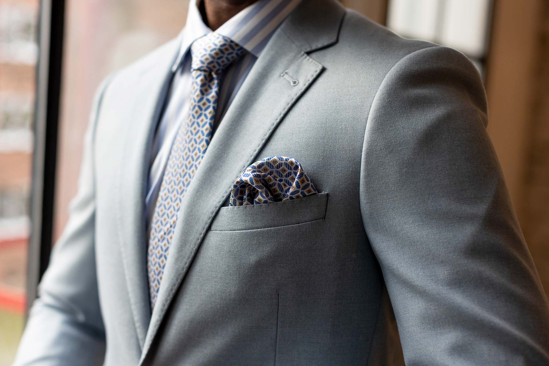Mann im grauen Anzug mit gemusterter Krawatte und Einstecktuch.