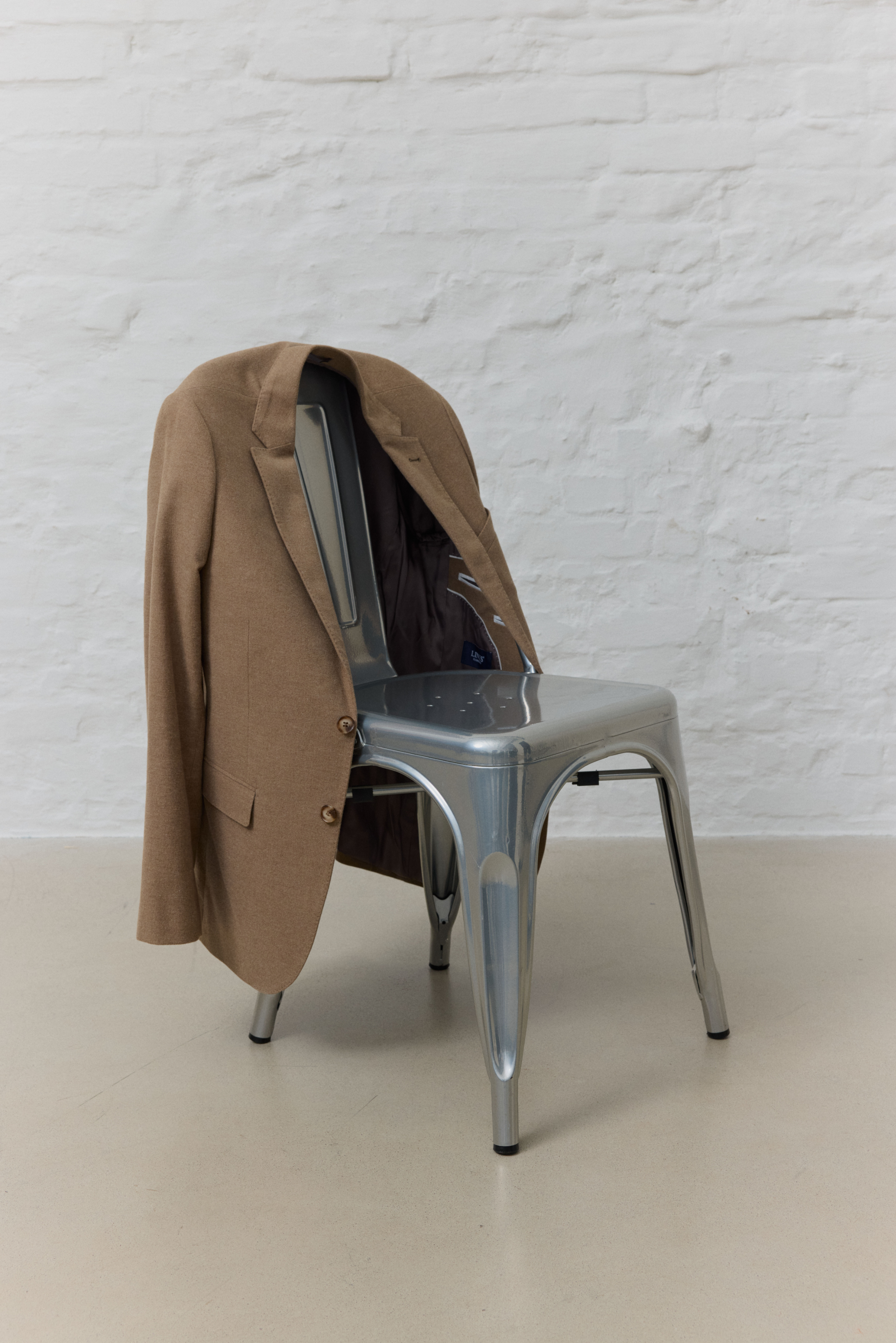 Brauner Herrenblazer hängt über silbernem Stuhl.