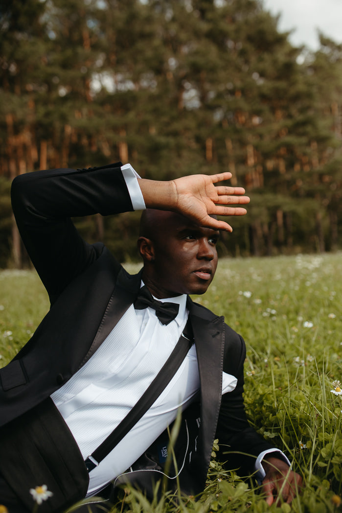 Mann im Anzug liegt auf Wiese, Hand über Stirn.