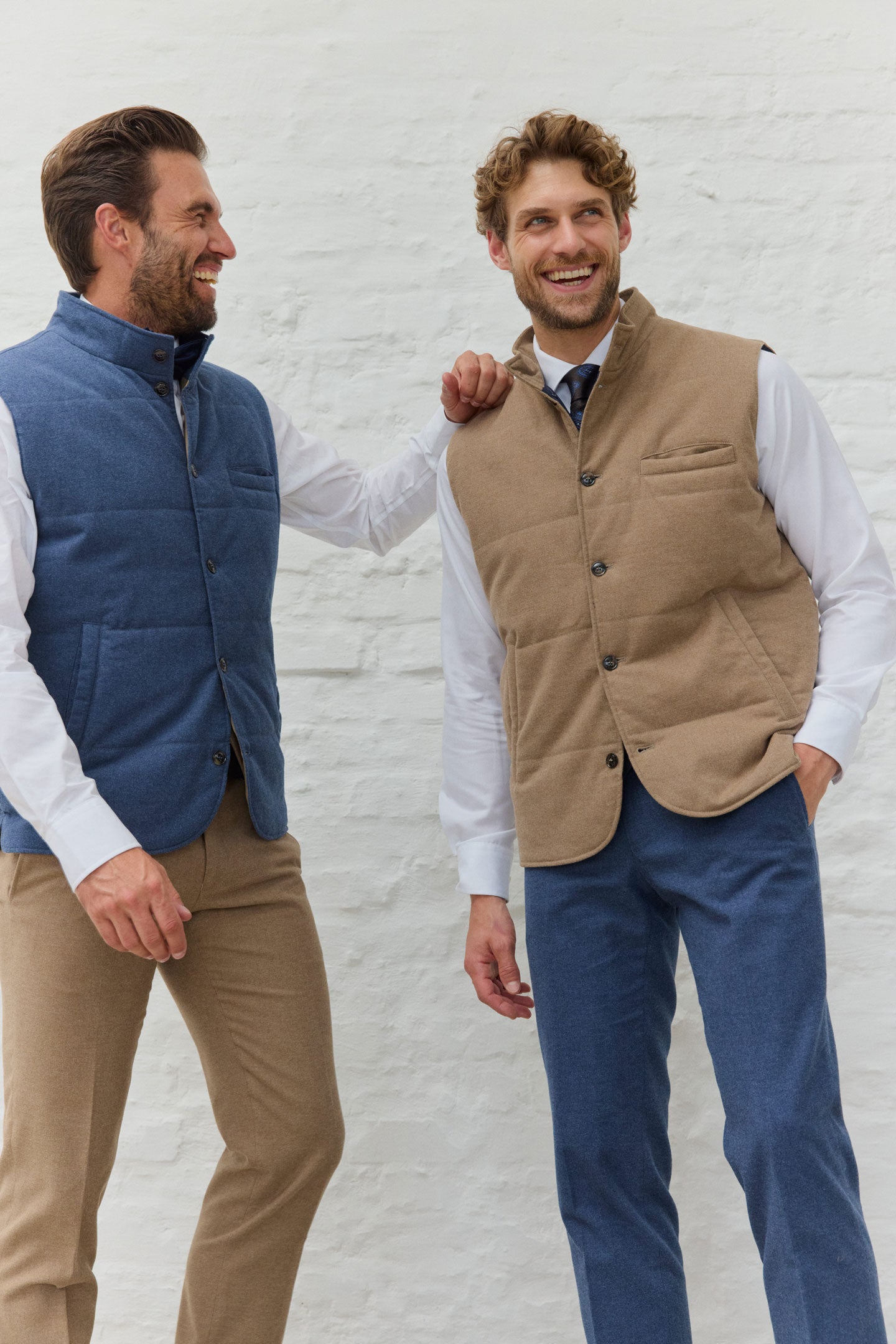 Zwei Männer in Westen und Hemden vor weißer Wand.