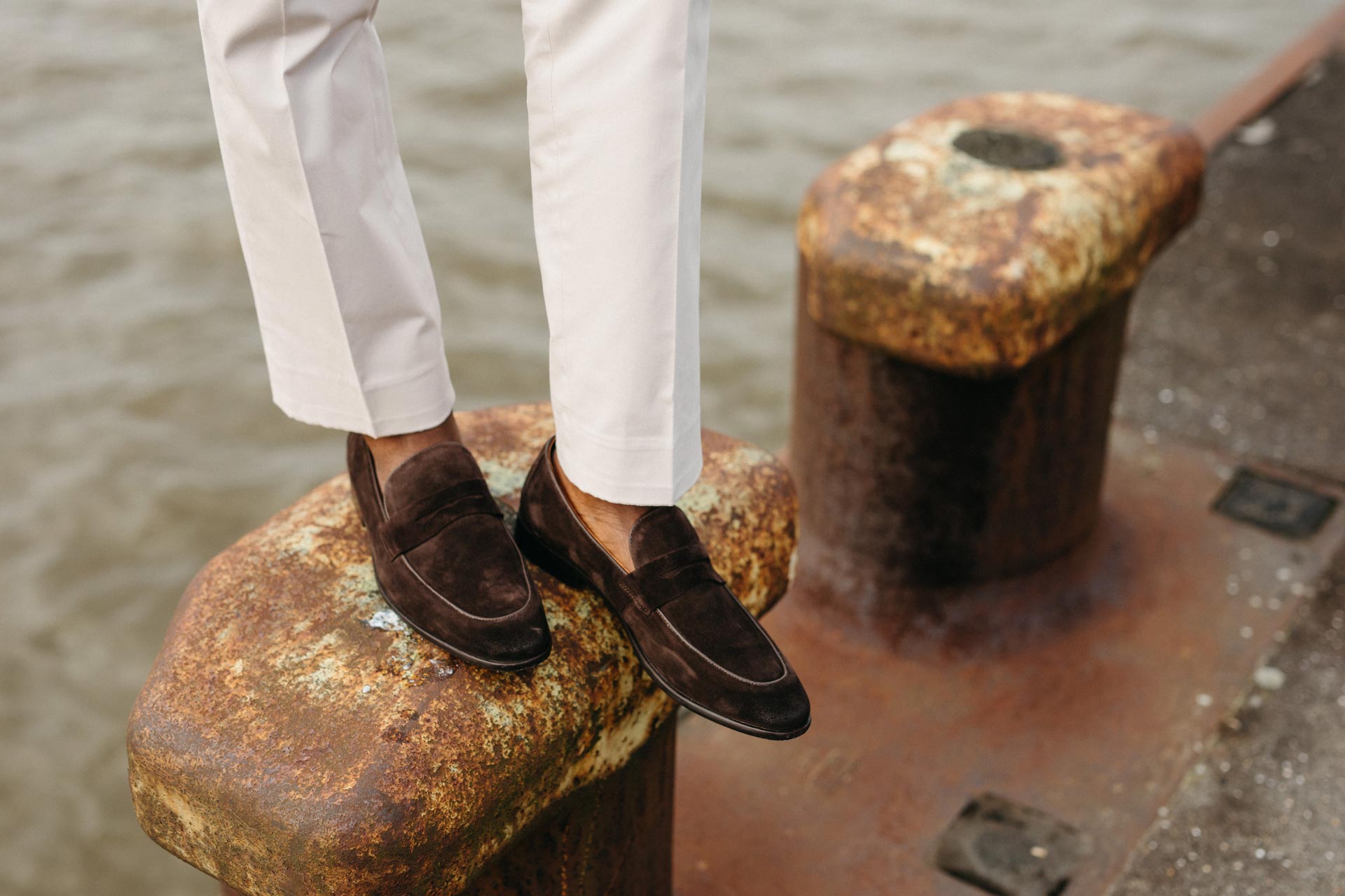 Mann trägt braune Loafer und weiße Hose am Wasser.