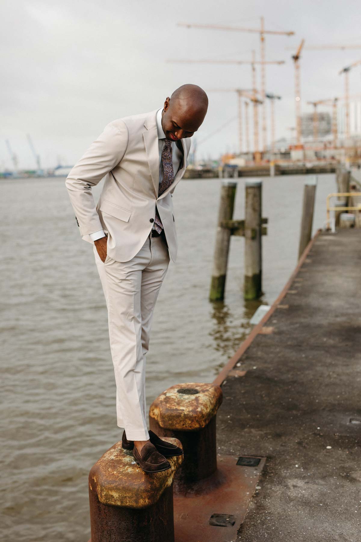Mann im Anzug steht auf Hafenkante, Kräne im Hintergrund.