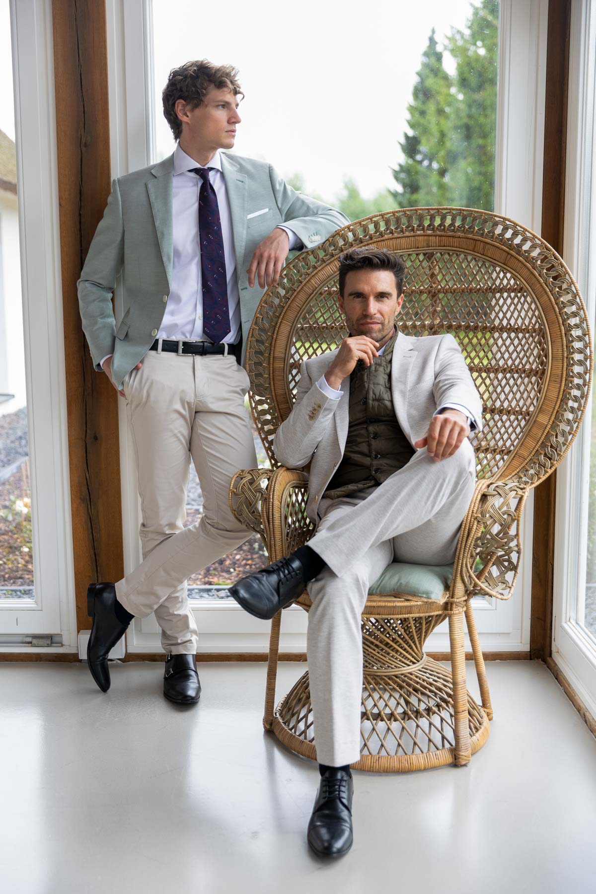 Zwei Männer in Anzügen, einer sitzt, einer steht.