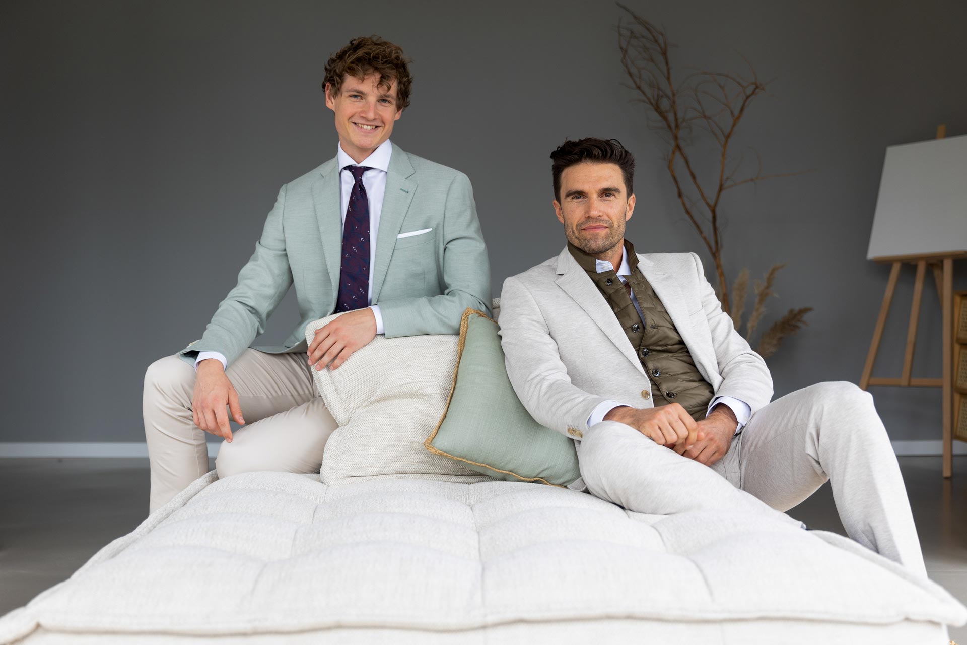 Zwei Männer in Anzügen sitzen auf einem Sofa.