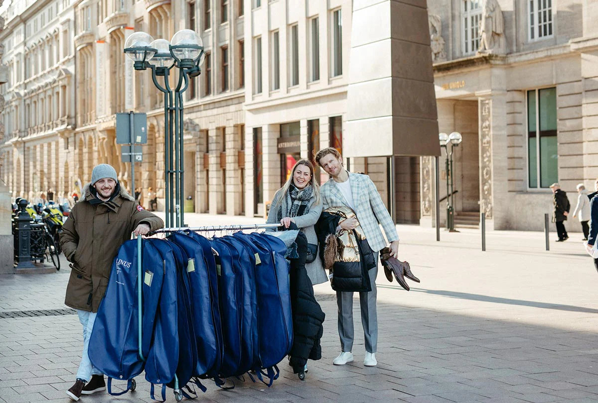 Drei Personen mit Kleiderhüllen auf einer Stadtstraße.