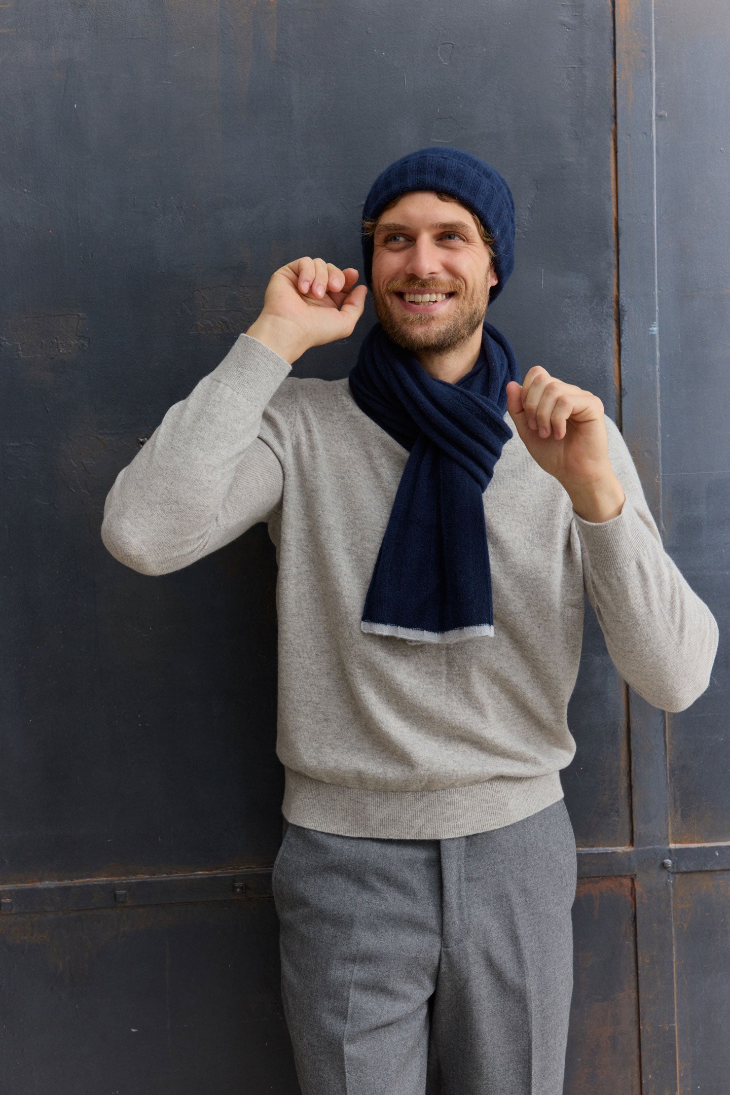 Mann trägt grauen Pullover, blaue Mütze und Schal.